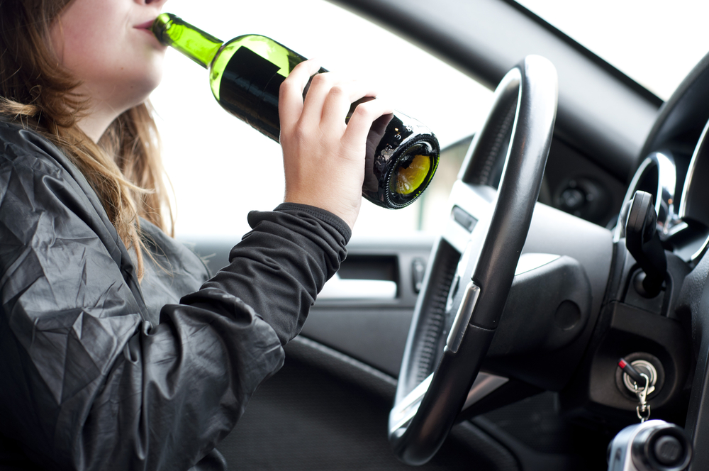 Young woman drinking alcohol while driving